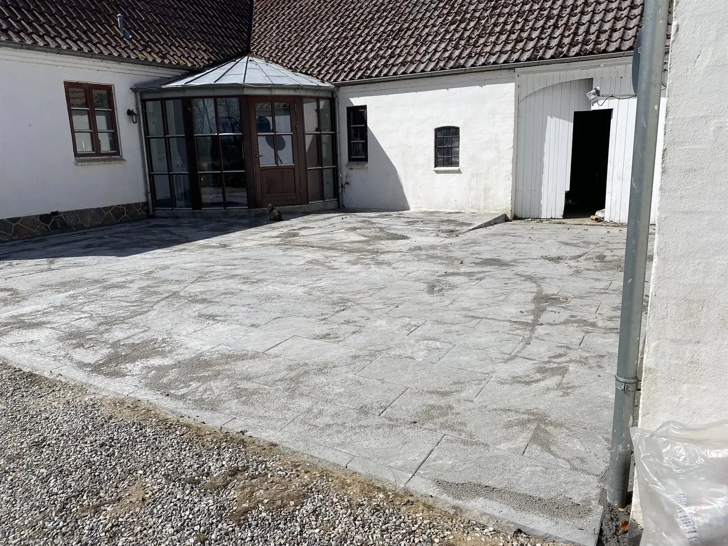 Nyrenset flisebelagt gårdsplads ved gammelt hvidt hus